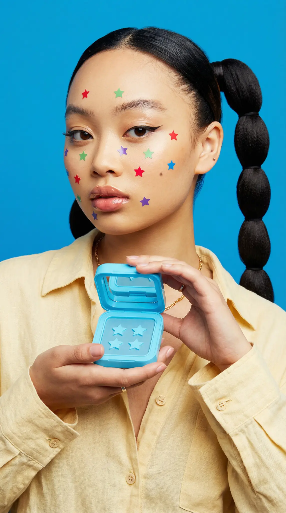 Starface acne patch campaign featuring model with colorful star stickers holding blue product case against bright blue background
