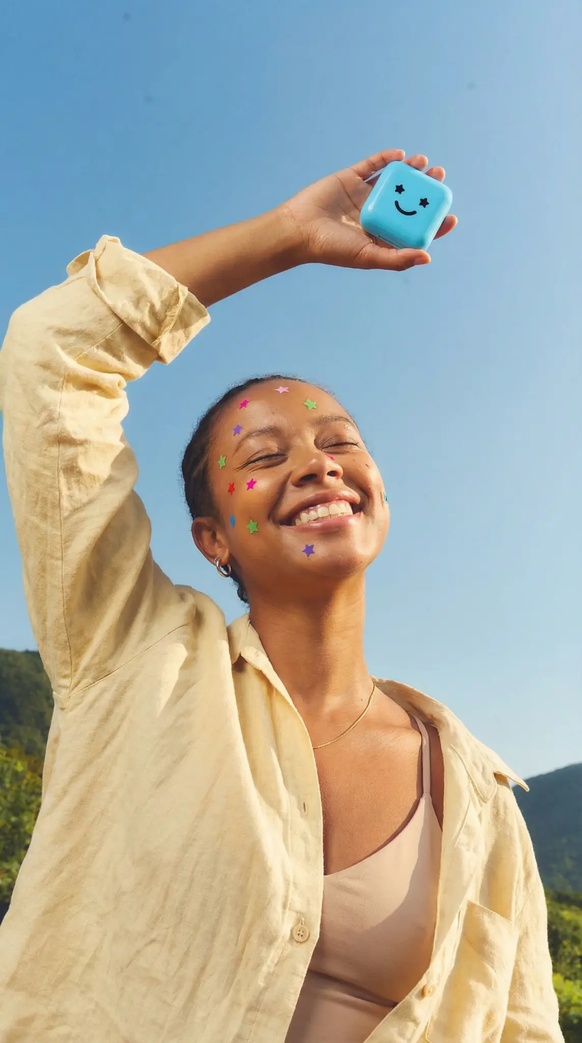 Starface outdoor lifestyle campaign with joyful model holding blue smiley face product case with colorful star patches